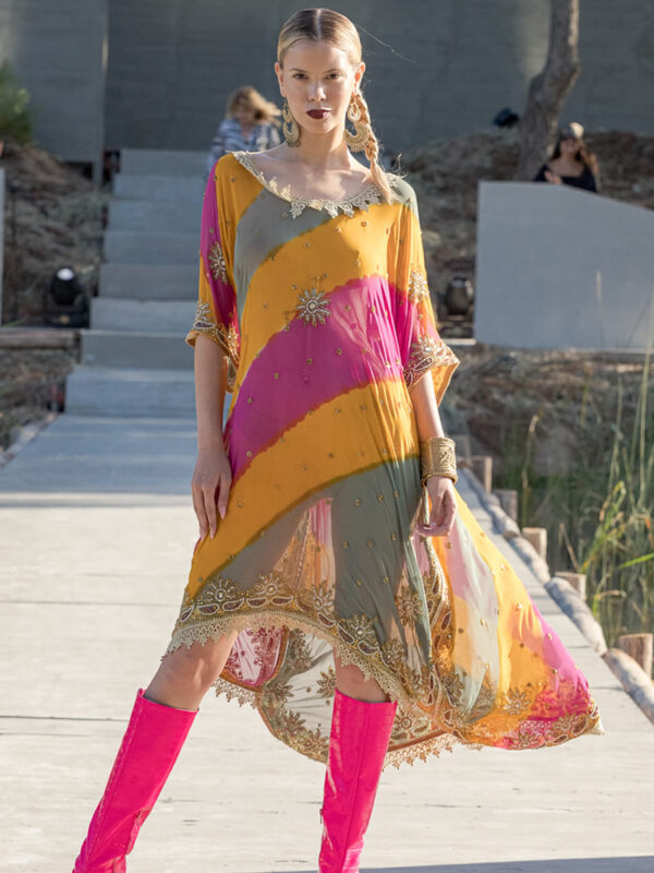 Mujer parada al final de pasarella, con un vestido en franjas de colores y bordados en piedras.